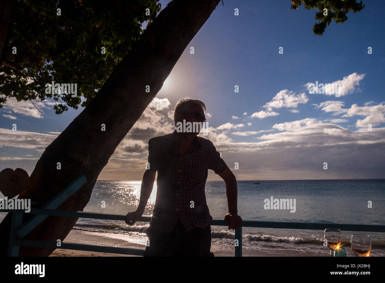 Un homme en silhouette est au-dessus de la plage de Bathsheba, la Barbade, en partie ombragée par un arbre. Banque D'Images