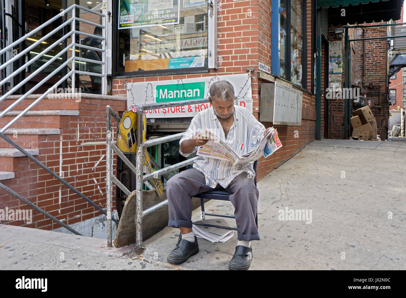 Un homme du Bangladesh lire un journal écrit en bengali sur 73ème rue à Jackson Heights. Queens, New York. Banque D'Images
