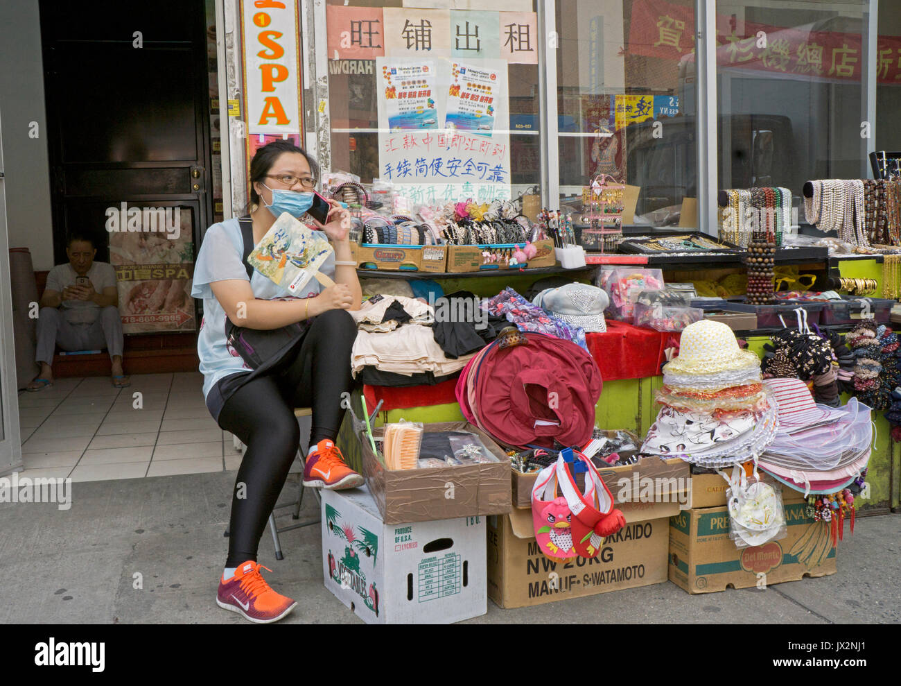 Une femme chinoise américaine regarde son magasin tout en parlant au téléphone et en se portant à Chinatown, Flushing, Queens, New York City Banque D'Images