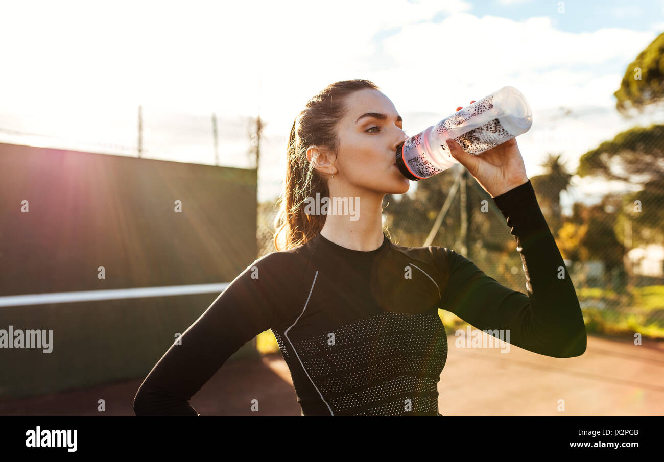 Portrait de belle jeune femme de l'eau potable après entraînement sur une journée ensoleillée. La sportive de prendre de pause après séance de formation sur le court de tennis. Banque D'Images