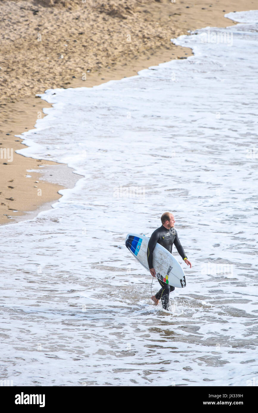UK Surf. Un surfeur dans la mer à pied dans Fistral Newquay, Cornwall. Banque D'Images
