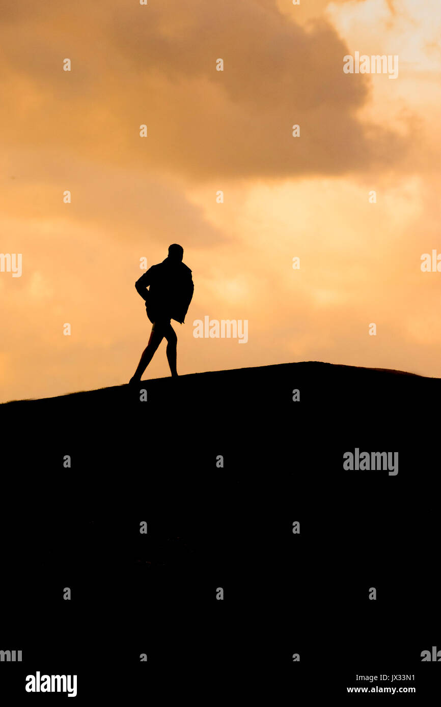 La silhouette d'un homme marchant sur une petite colline au coucher du soleil. Banque D'Images