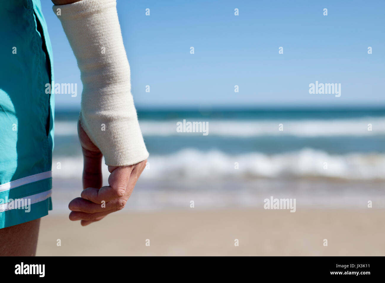 Libre d'un jeune homme de race blanche en maillot de bain sur la plage avec un bandage à son poignet, en face de la mer, avec un espace négatif sur la droite Banque D'Images