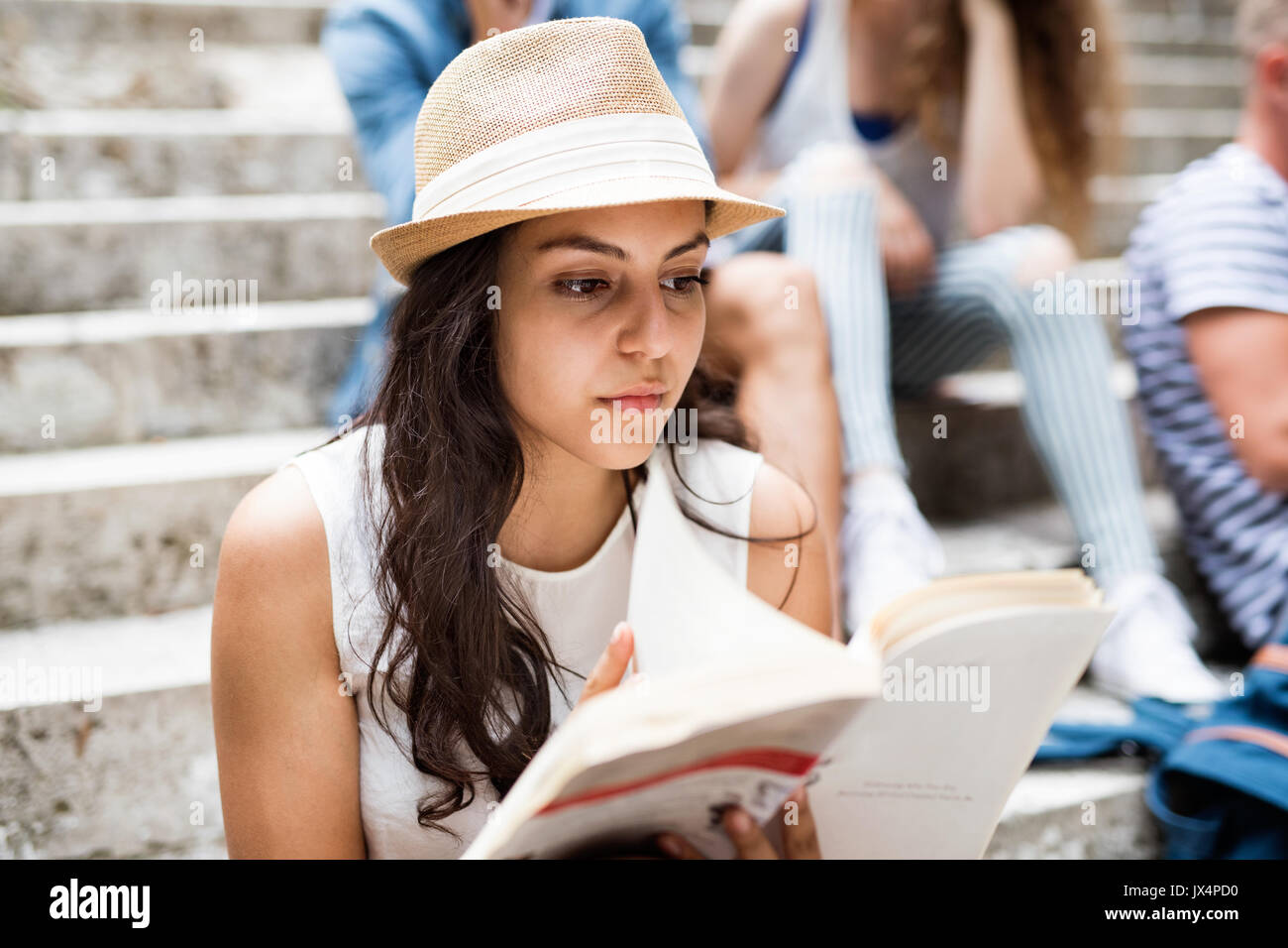 Teenage student attrayant fille assise sur des marches en pierre avec ses amis en face de l'université de la lecture d'un livre. Banque D'Images