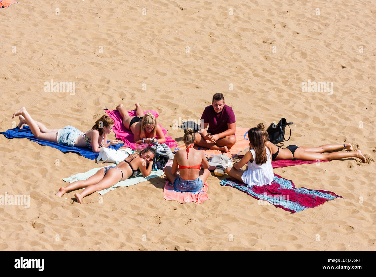 Canicule, Groupe d'adolescents réunis en cercle, principalement des jeunes femmes en bikini, portant sur des serviettes de plage. Vue à distance, angle élevé. Banque D'Images Canicule, Groupe d'adolescents réunis en cercle, principalement des jeunes femmes en bikini, portant sur des serviettes de plage. Vue à distance, angle élevé. Banque D'Images