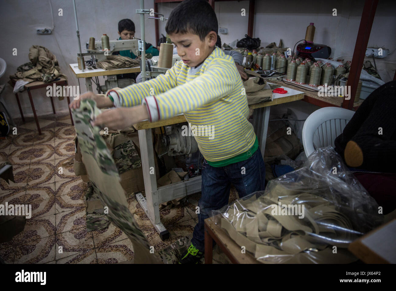 L'un des innombrables nombre d'enfants syriens réfugiés travaillant dans des usines à travers la Turquie, maintenant plus de 2,7 millions de Syriens. La petite boutique textile où lui et d'autres garçons, filles et les hommes sont employés produit des uniformes militaires et des sacs à dos qui sont vendues aux différentes factions en Syrie. La pauvreté conduit de nombreuses familles à envoyer leurs enfants au travail au lieu de à l'école. Les possibilités d'éducation pour les Syriens en Turquie sont également limitées. Banque D'Images