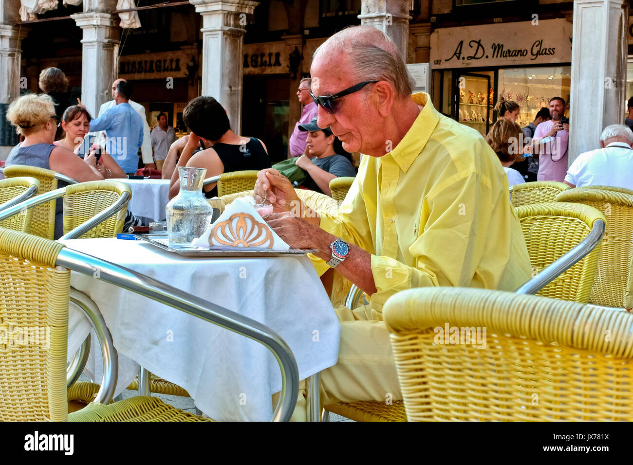 Smart Personnes âgées gentleman habillé en jaune la consommation de crème glacée au café en plein air avec chaises et nappes jaune. Vieil homme. La Place Saint Marc Venise Italie Banque D'Images