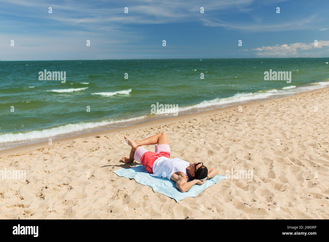 Happy smiling young man sunbathing on beach towel Banque D'Images