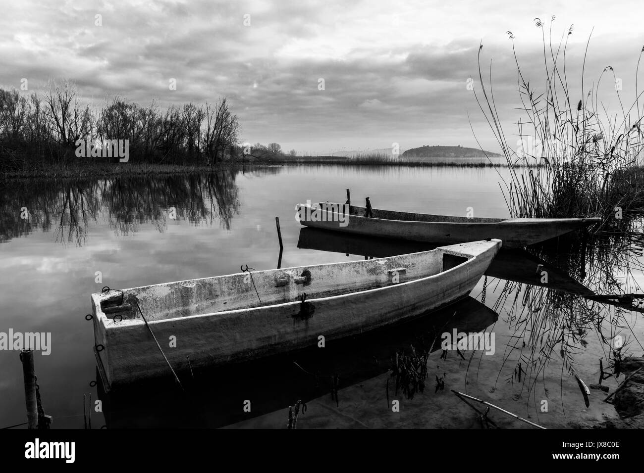 Quelques petits bateaux de pêche sur un lac au coucher du soleil, avec presque beau ciel et nuages reflets sur l'eau encore Banque D'Images