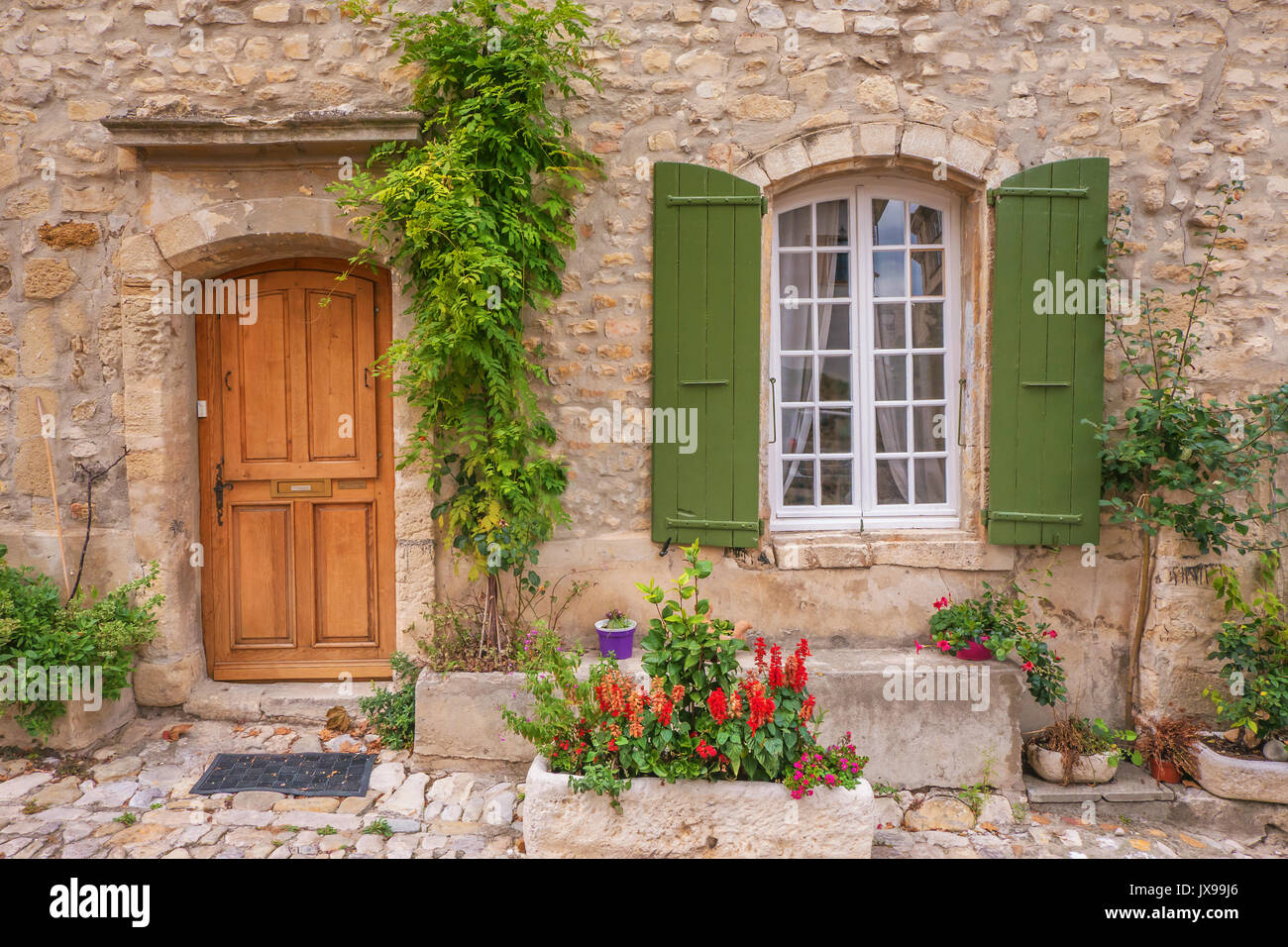 Street View de vieille maison en pierre en façade avec une porte en bois, porte-fenêtre à volets, et colorés de plantes en pot. Provence, France. Banque D'Images