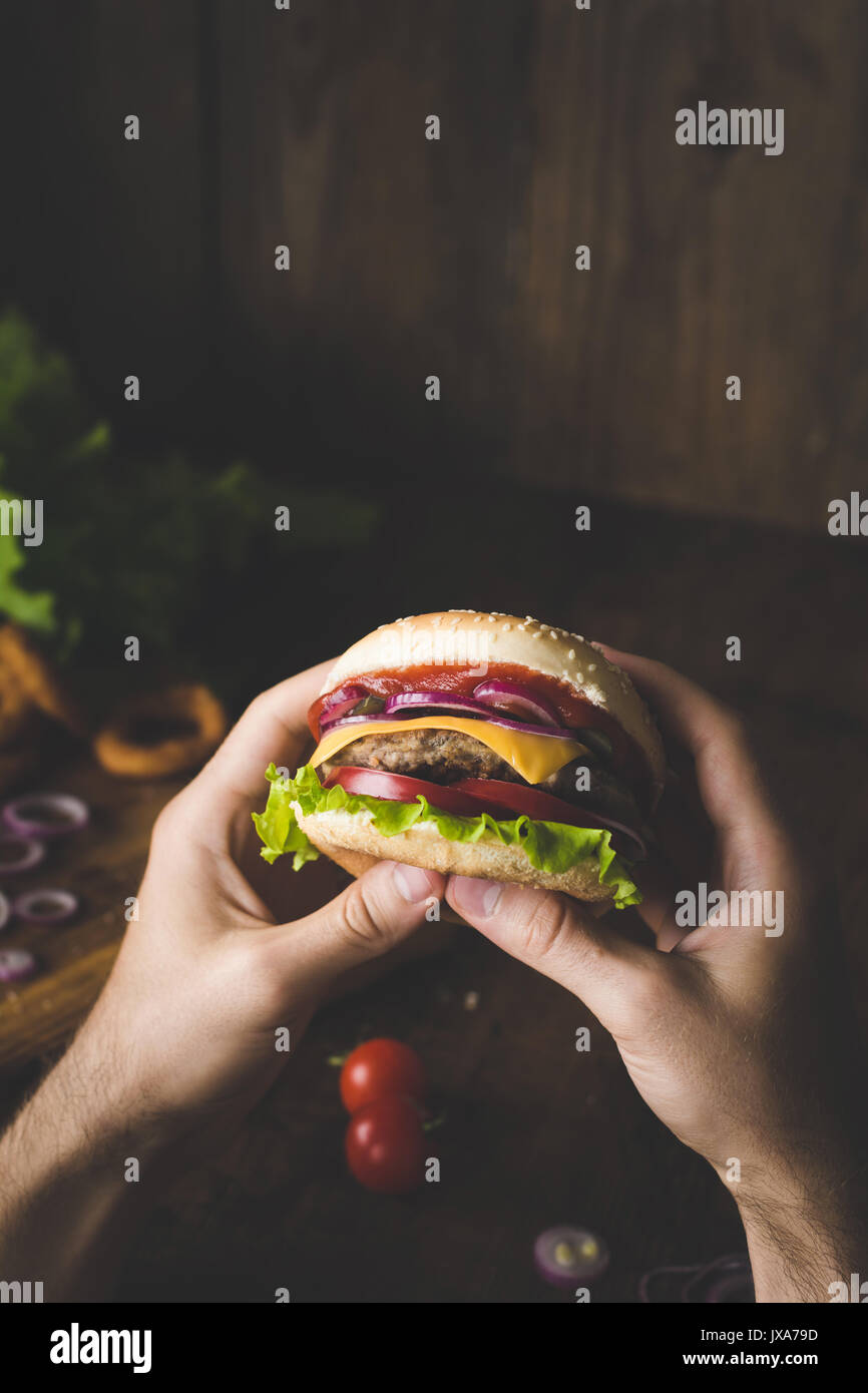 Man eating cheeseburger. Hands holding cheeseburger vue rapprochée selective focus Banque D'Images