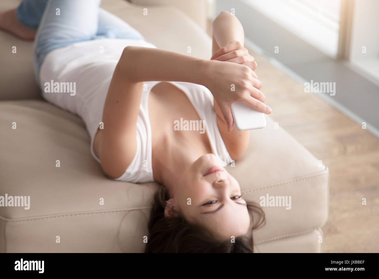 Young woman lying on sofa using mobile phone selfies, en tenant Banque D'Images