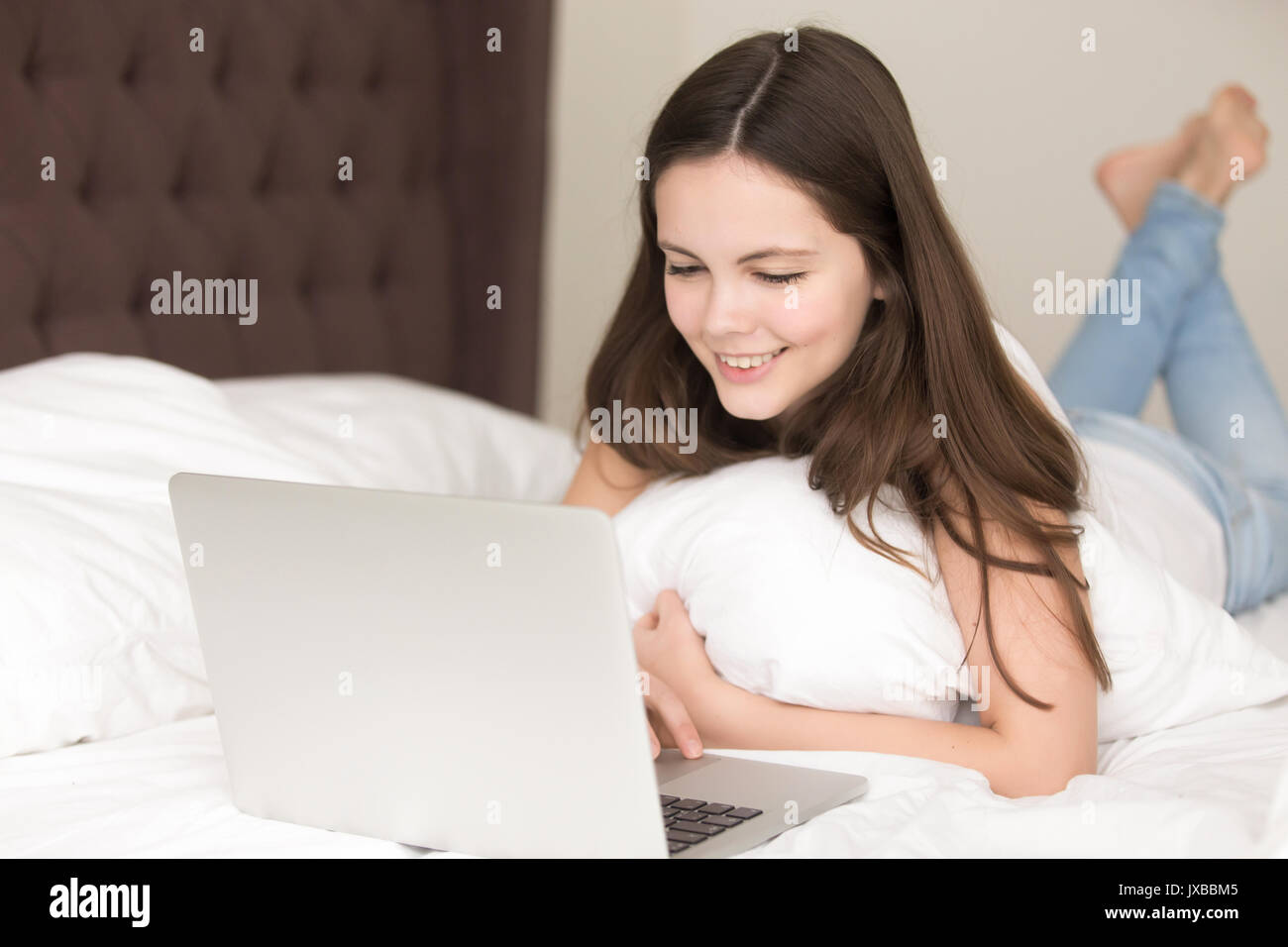 Smiling young lady en utilisant laptop lying on bed, communiquer onli Banque D'Images