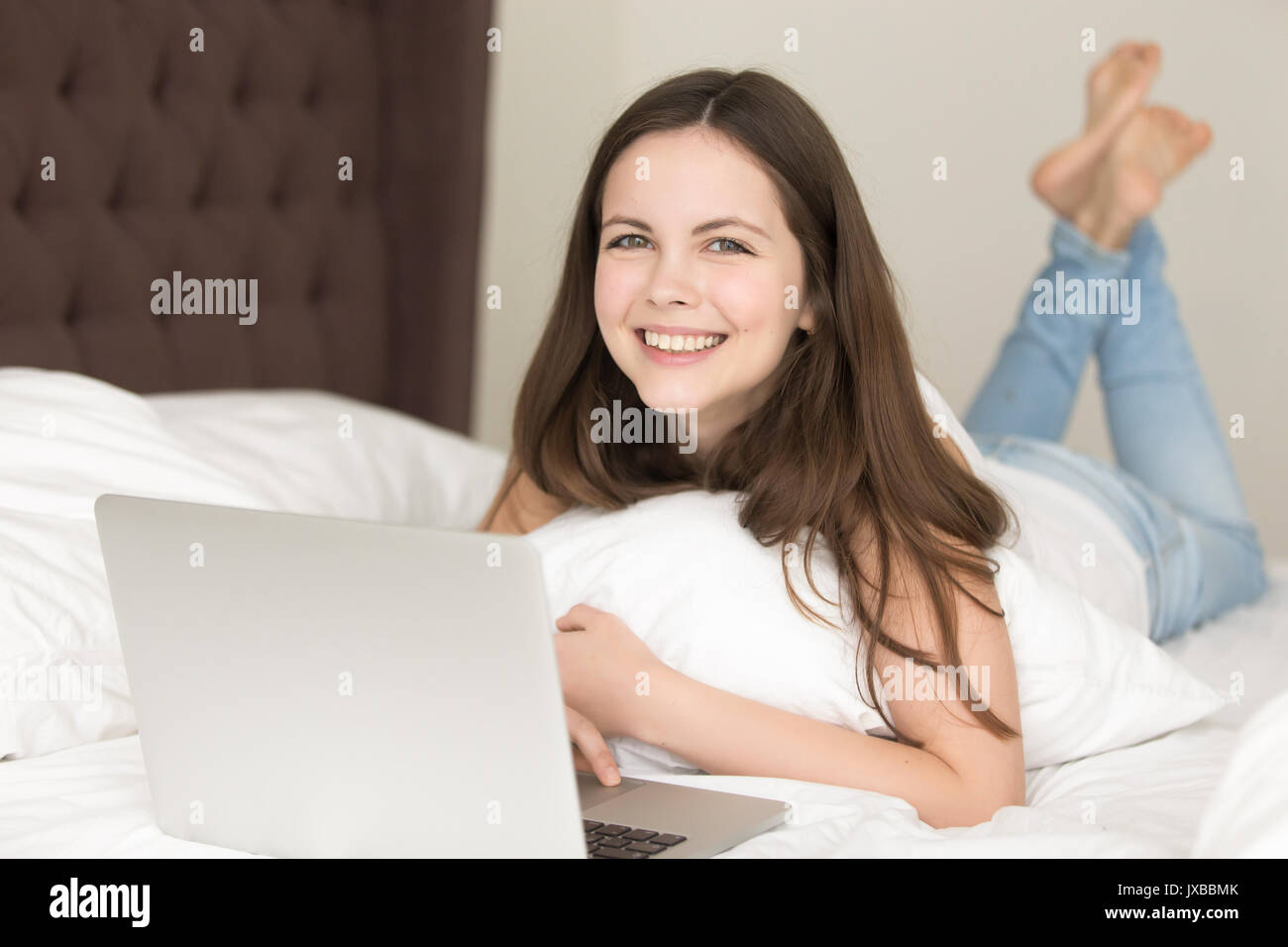 Jeune femme avec un ordinateur portable sur lit, bénéficiant de temps à la maison Banque D'Images