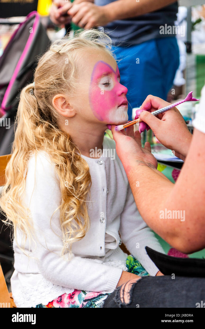 Portrait enfant blonde, fille, 7-8 ans, vue de côté, avoir peint en rose face à face de chat. Main tenant son menton, l'autre main tenant un pinceau. Banque D'Images