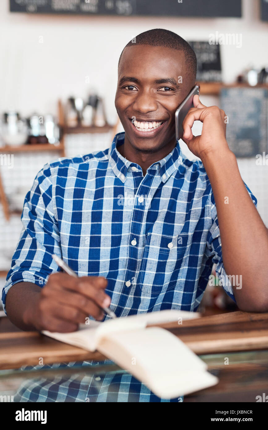 Smiling young entrepreneur l'utilisation d'un cellulaire dans son cafe Banque D'Images