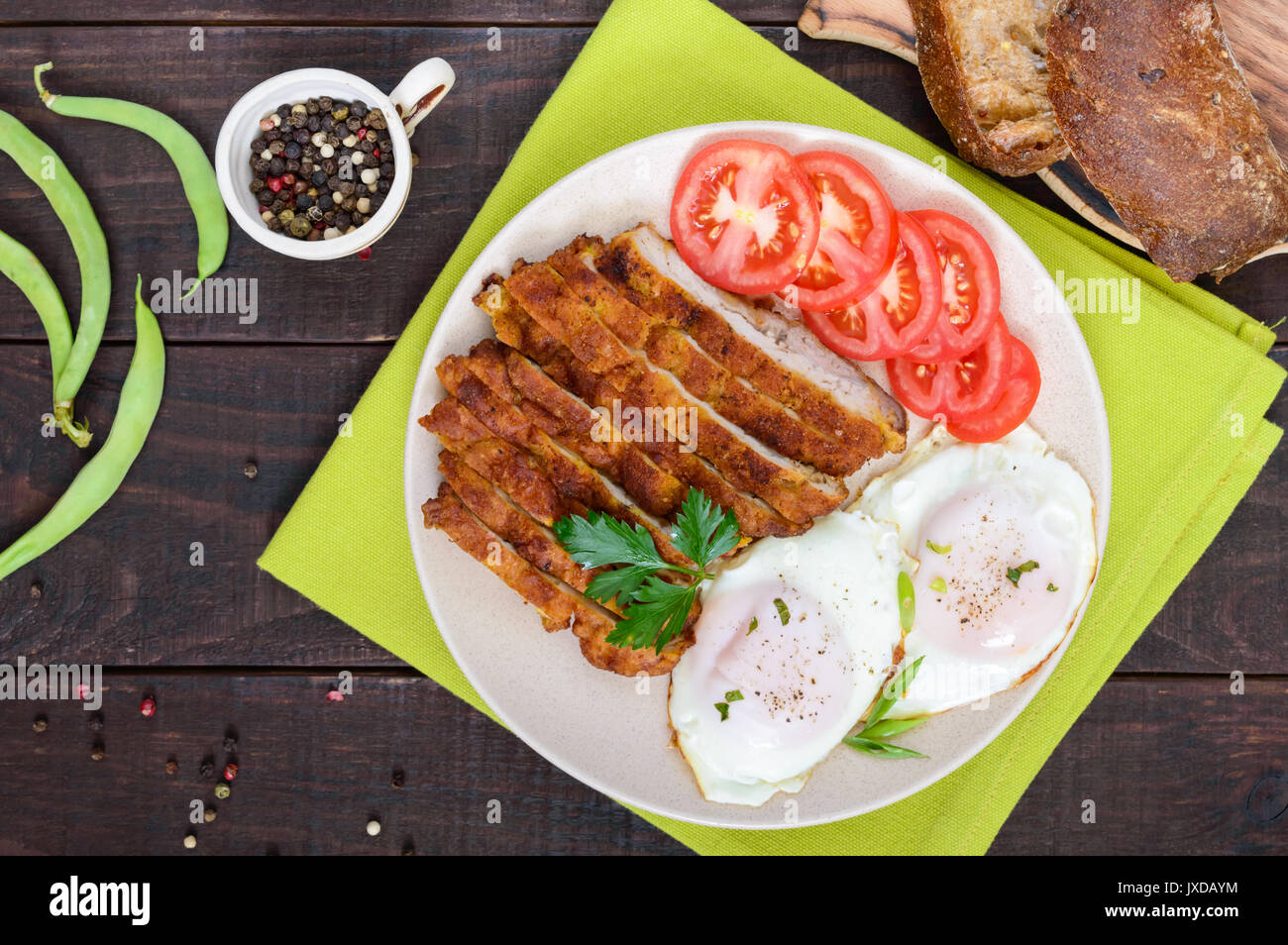 Morceaux de chop (schnitzel), pain grillé avec des oeufs, la tomate fraîche sur un fond de bois sombre. Vue d'en haut. Banque D'Images