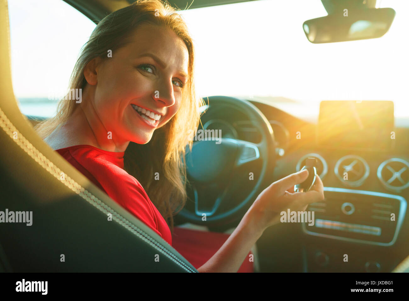 Femme heureuse dans une robe rouge avec une clé dans sa main est assis dans la voiture. Le concept de l'achat ou la location d'une voiture Banque D'Images