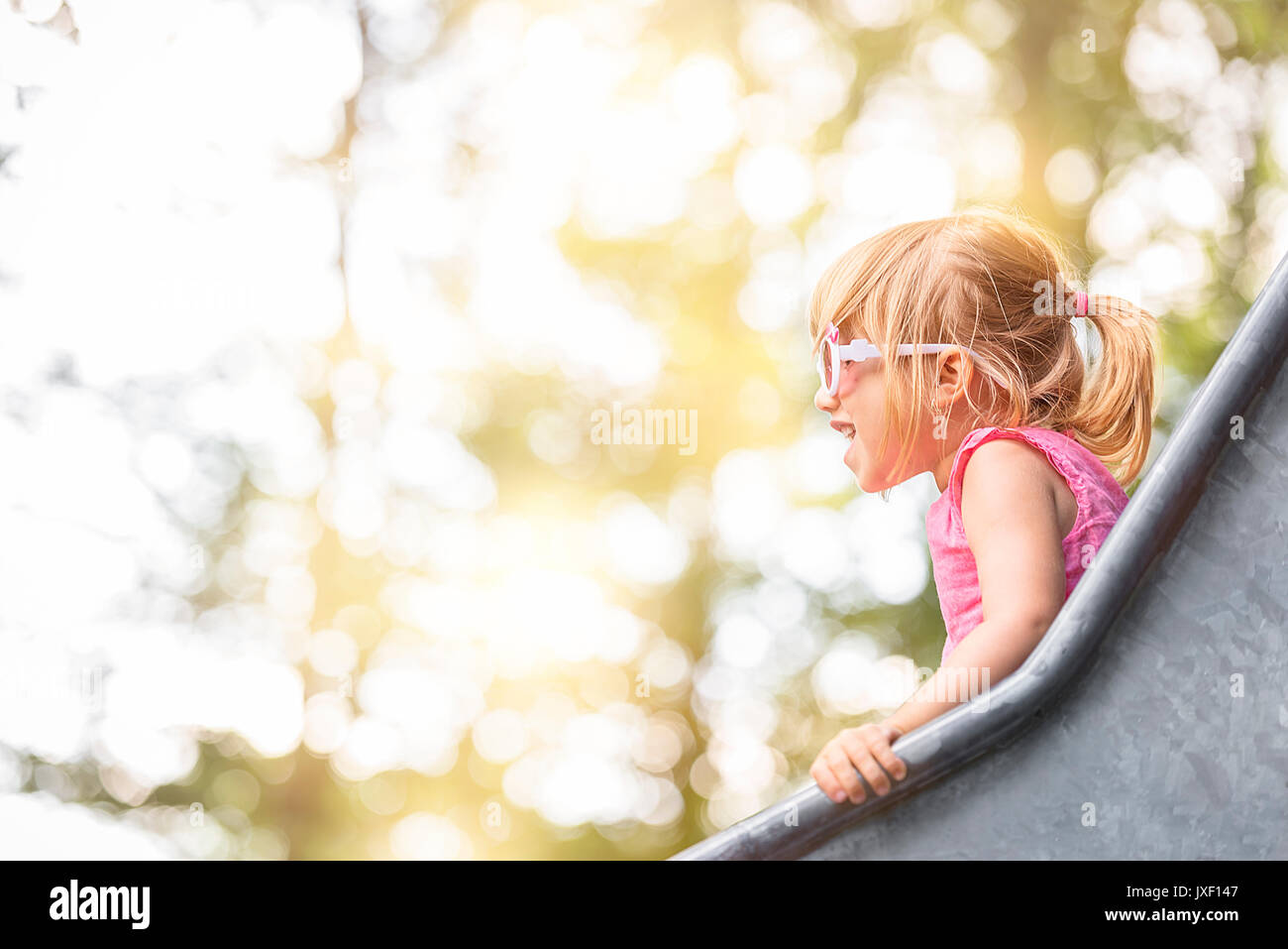 Image en gros plan avec une petite fille s'amusant sur une diapositive à partir d'une aire de jeux, sur une journée ensoleillée. Banque D'Images