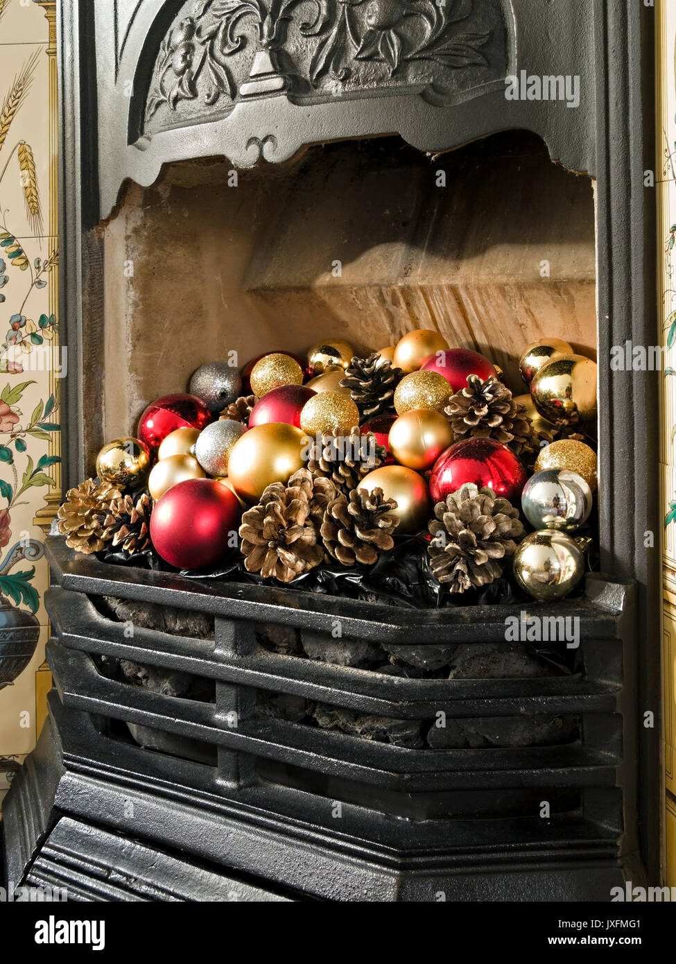 Jolie cheminée en fonte de style victorien et grille décorée de boules de Noël colorées et de cônes de sapin, Angleterre, Royaume-Uni Banque D'Images