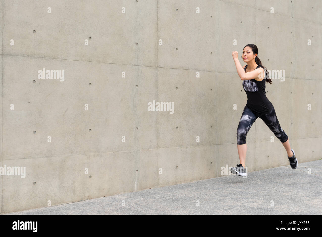 Vue latérale photo de female runner tournant sur fond de mur gris trottoir en matinée pour la formation force explosive et personnels à holida Banque D'Images