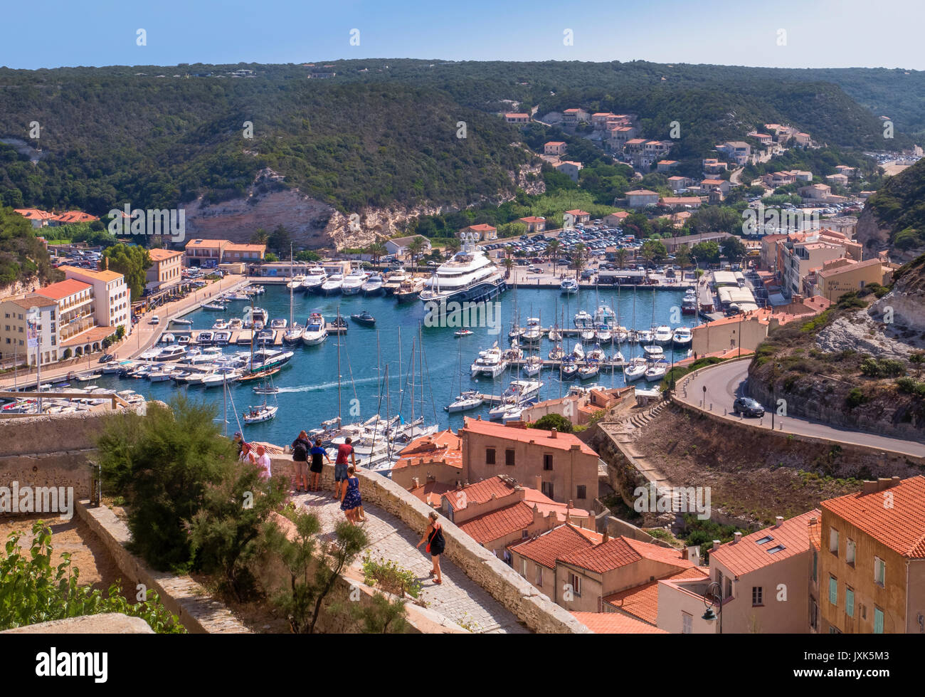 Vue aérienne du port de Bonifacio entourée de maisons, routes sinueuses et de collines vertes au-dessus, la Corse du Sud, France Banque D'Images