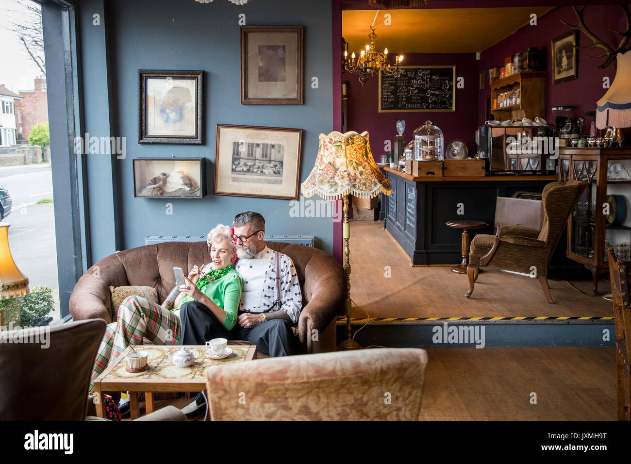 Quirky vintage couple looking at smartphone dans les salons de thé Banque D'Images