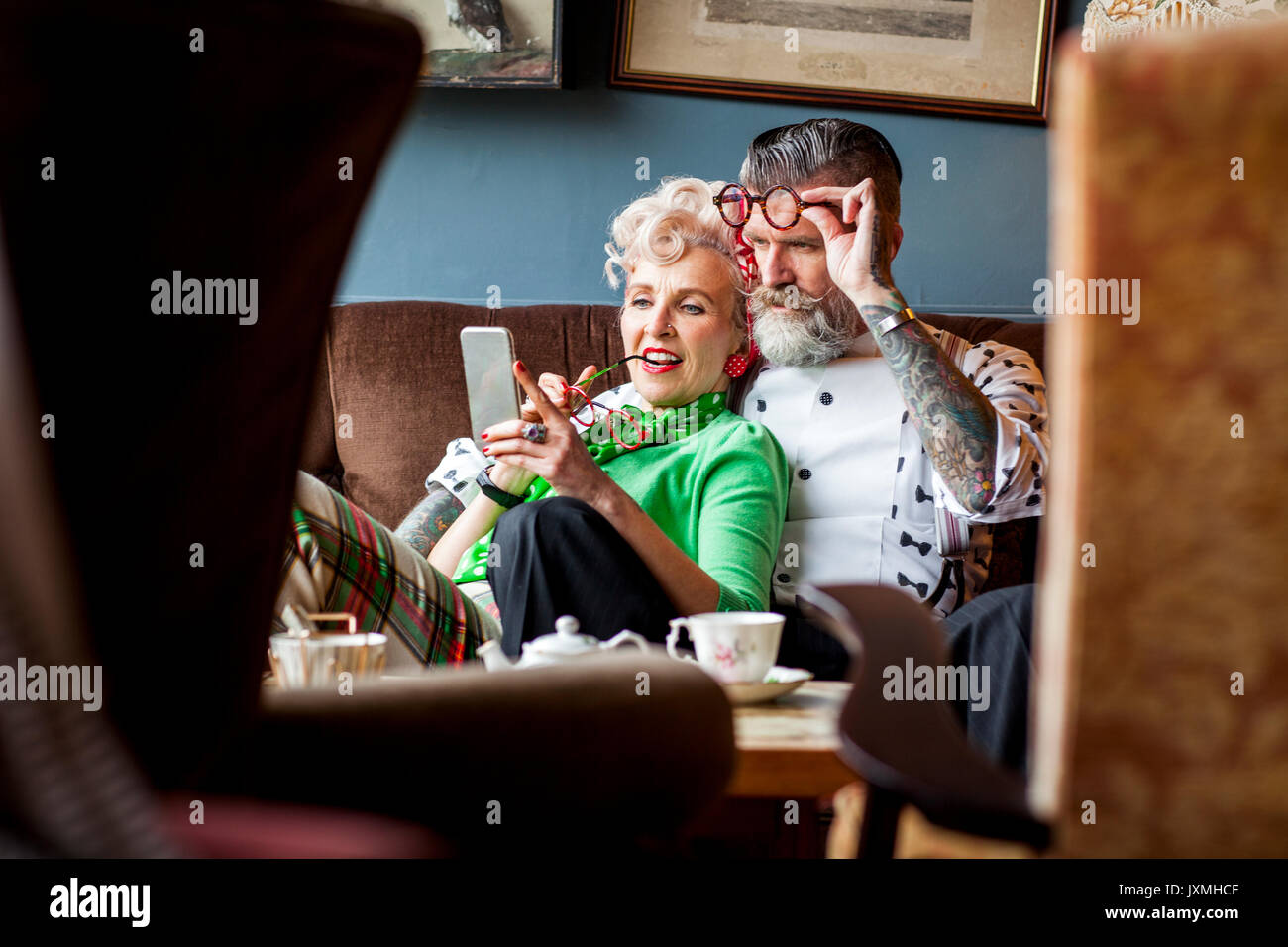 Quirky vintage couple looking at smartphone in salon de thé Banque D'Images