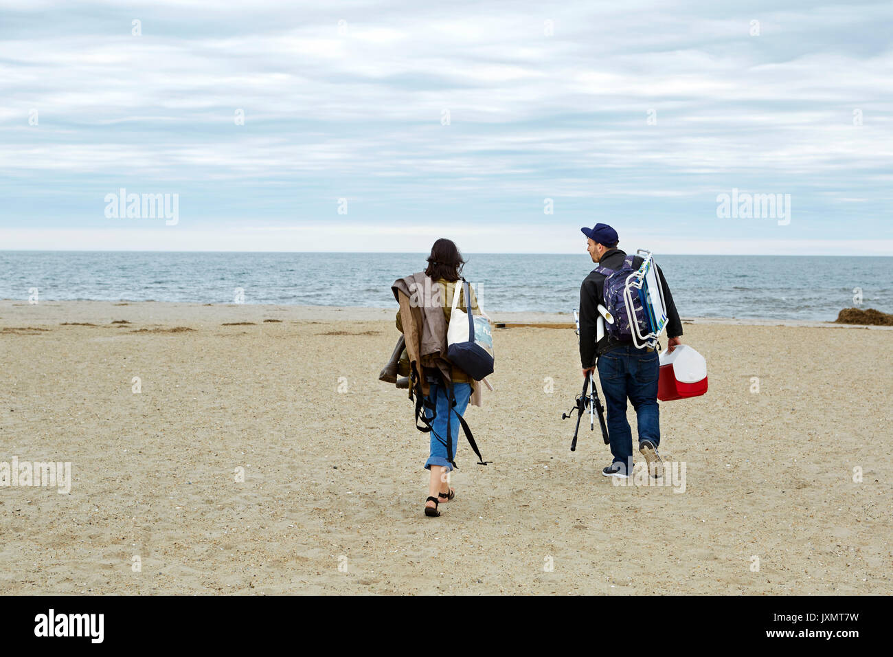 Vue arrière du jeune couple transportant du matériel de pêche en mer sur la plage Banque D'Images