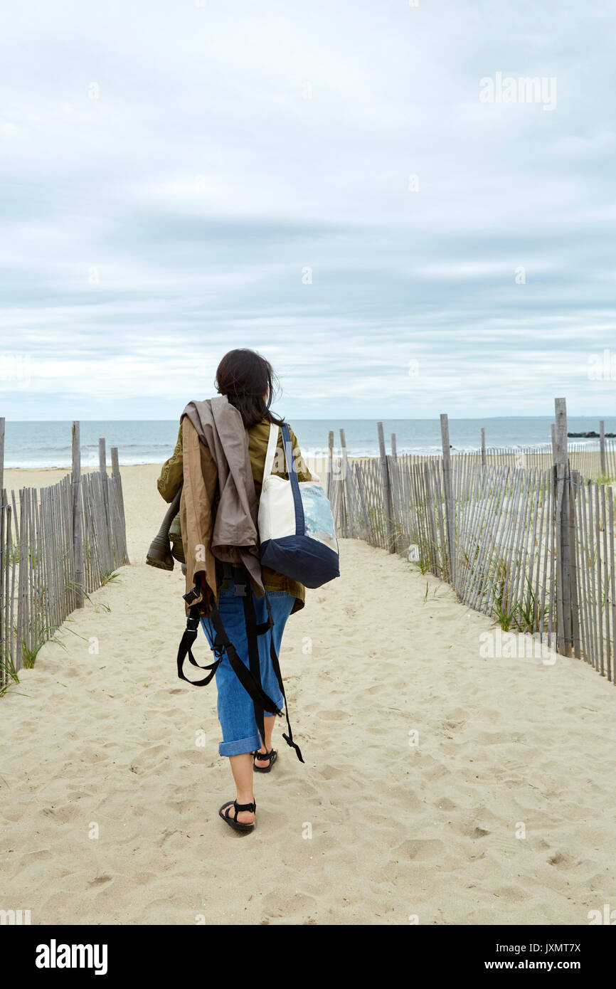 Vue arrière du Jeune femme transportant du matériel de pêche en mer sur la plage Banque D'Images