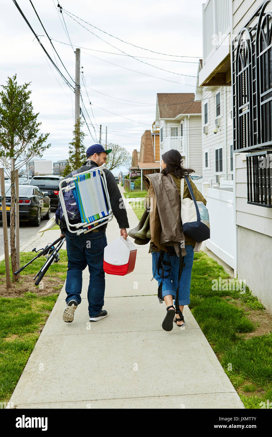Vue arrière du jeune couple transportant du matériel de pêche sur le trottoir Banque D'Images