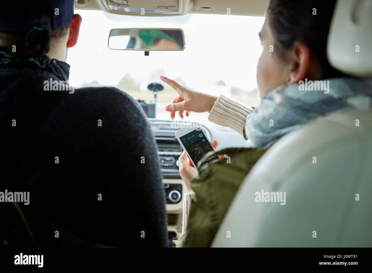 Young couple sitting in car, woman holding smartphone, pointant les directions, vue arrière Banque D'Images