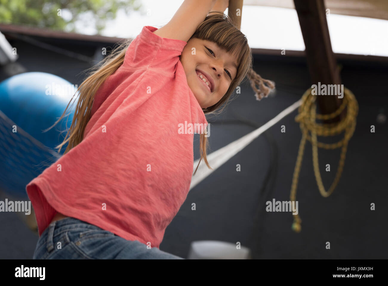 Girl hanging on Monkey bar regardant le sourire de l'appareil photo Banque D'Images