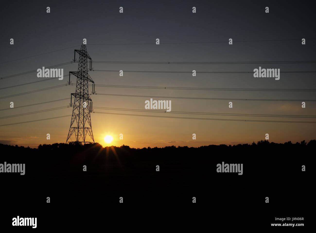 Le soleil se couche à côté d'un pylône de l'électricité en laissant la tour découpé sur un ciel orange Banque D'Images