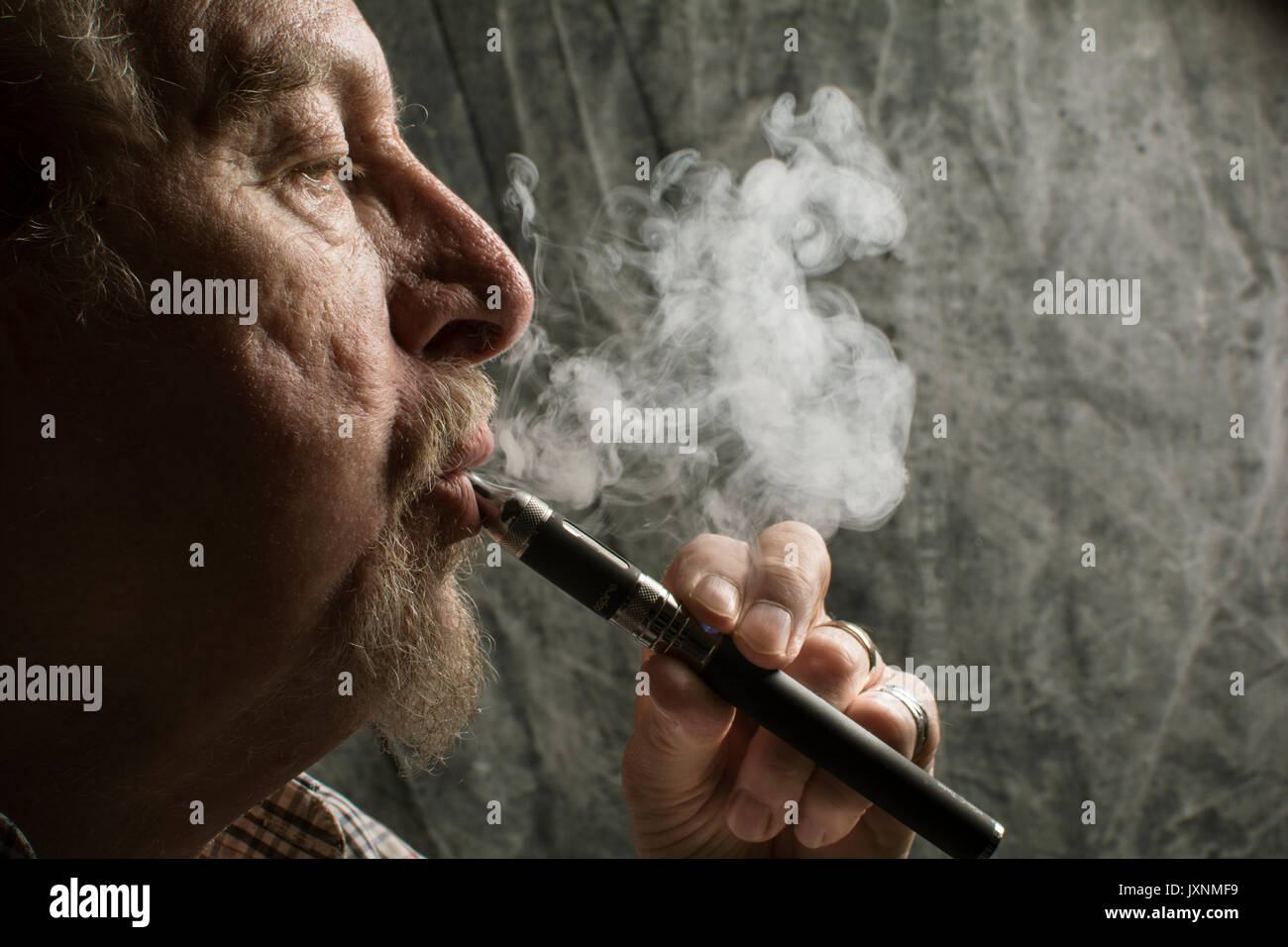 Un homme âgé, avec une barbe de fumer une cigarette électronique ( seine un e-cigarette), une option plus saine que le tabac des cigarettes. Banque D'Images