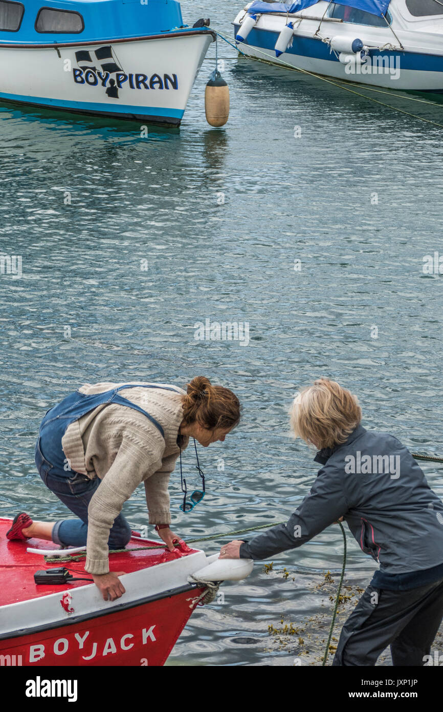 Deux femmes d'âge moyen, les amis de la navigation de plaisance dans le processus d'amarrage d'un petit bateau dans le port de Penzance. Cornwall, Angleterre, Royaume-Uni. Banque D'Images