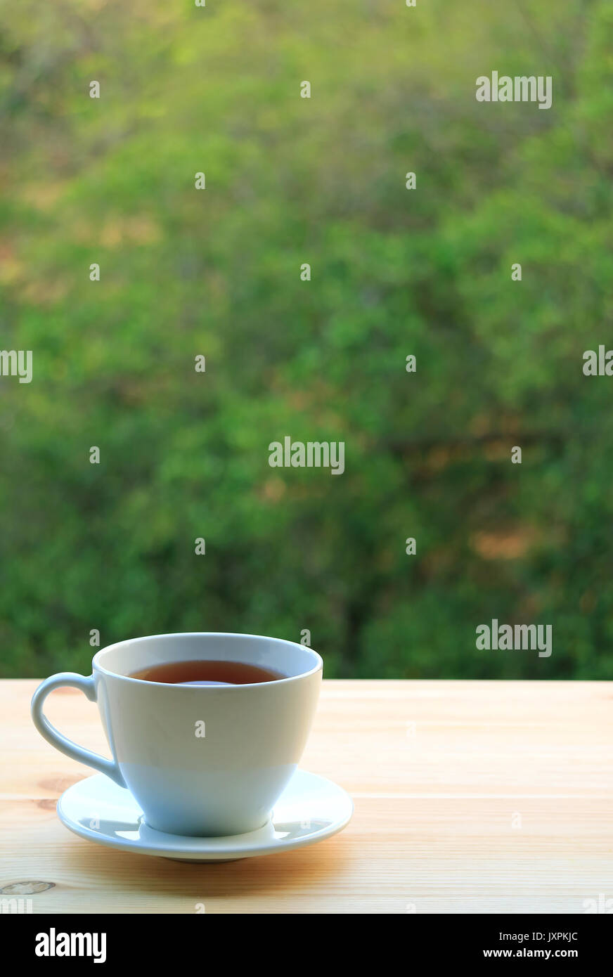 Une tasse de thé chaud servi sur table en bois par la fenêtre, avec l'arrière-plan flou de Grand Arbre Vert Banque D'Images