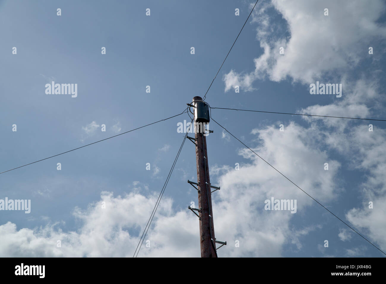 Haut d'un poteau télégraphique contre un ciel bleu avec des nuages blancs en Angleterre, Royaume-Uni Banque D'Images