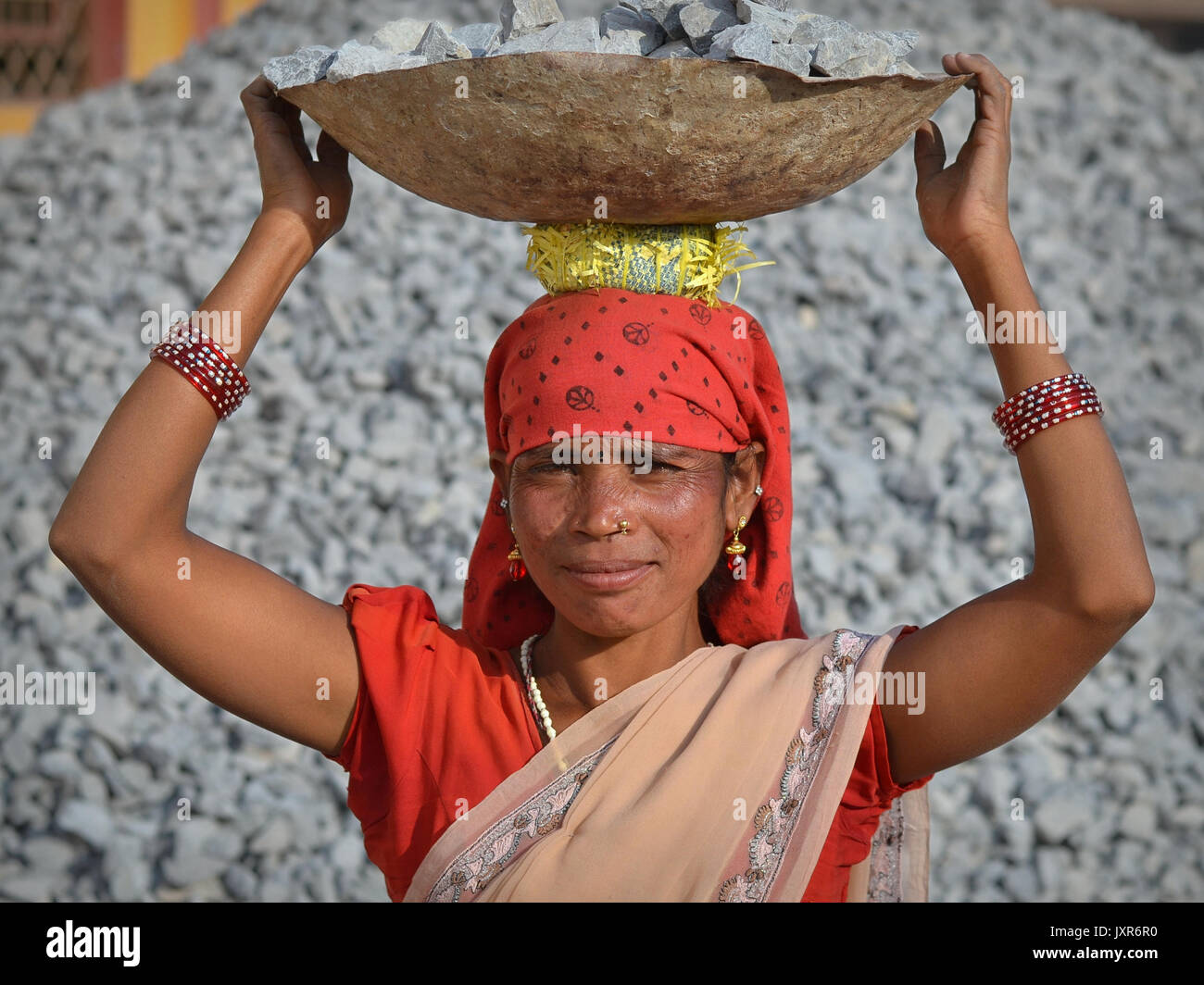 La femme tribale indienne Adevasi porte sur sa tête un bol en métal avec des roches écrasées pour la construction de routes. Banque D'Images