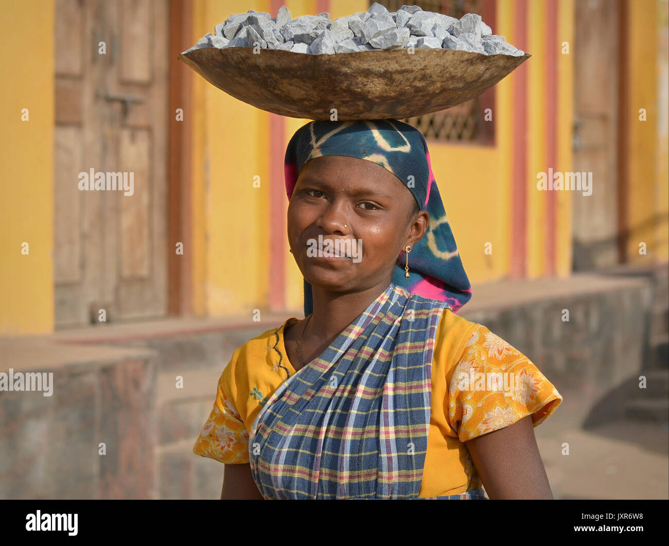 La jeune femme tribale indienne Adevasi équilibre sur sa tête un bol en métal avec des roches écrasées pour la construction de routes. Banque D'Images