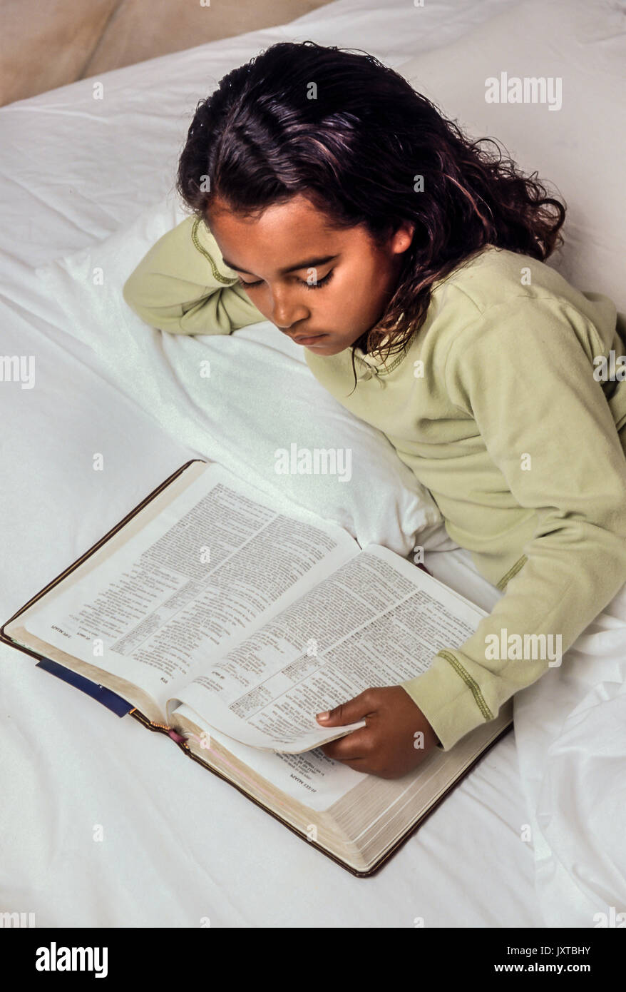Enfance enfant ethnique reading Bible au lit Jeune Fille 7-10 ans Africain/Caucasian United States Myrleen Pearson Banque D'Images