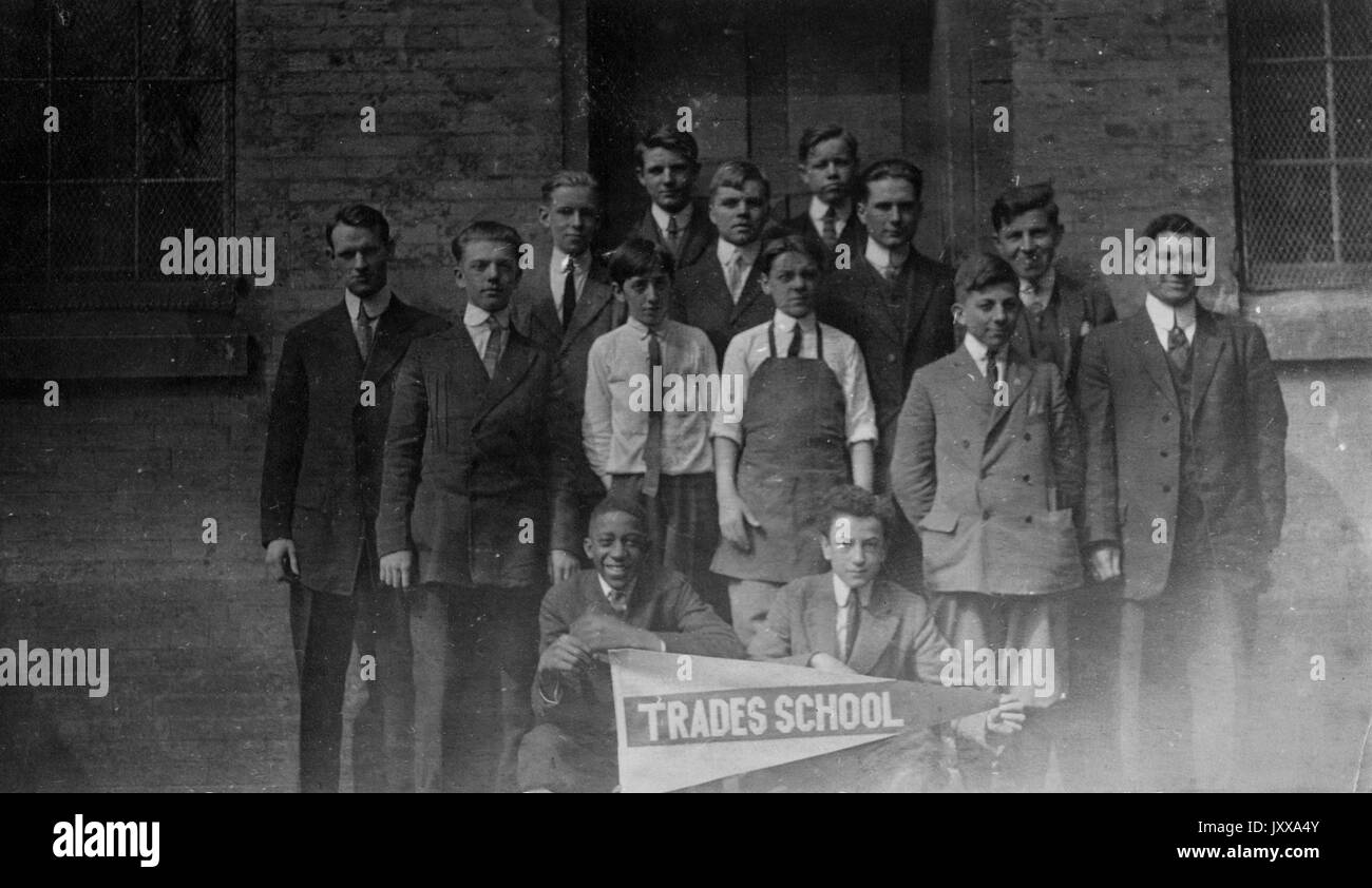 Photo de paysage pleine longueur d'un petit groupe de lycéens, deux assis tenant un panneau qui dit 'Trades School' dont un est un garçon afro-américain, d'autres debout derrière, 1910. Banque D'Images