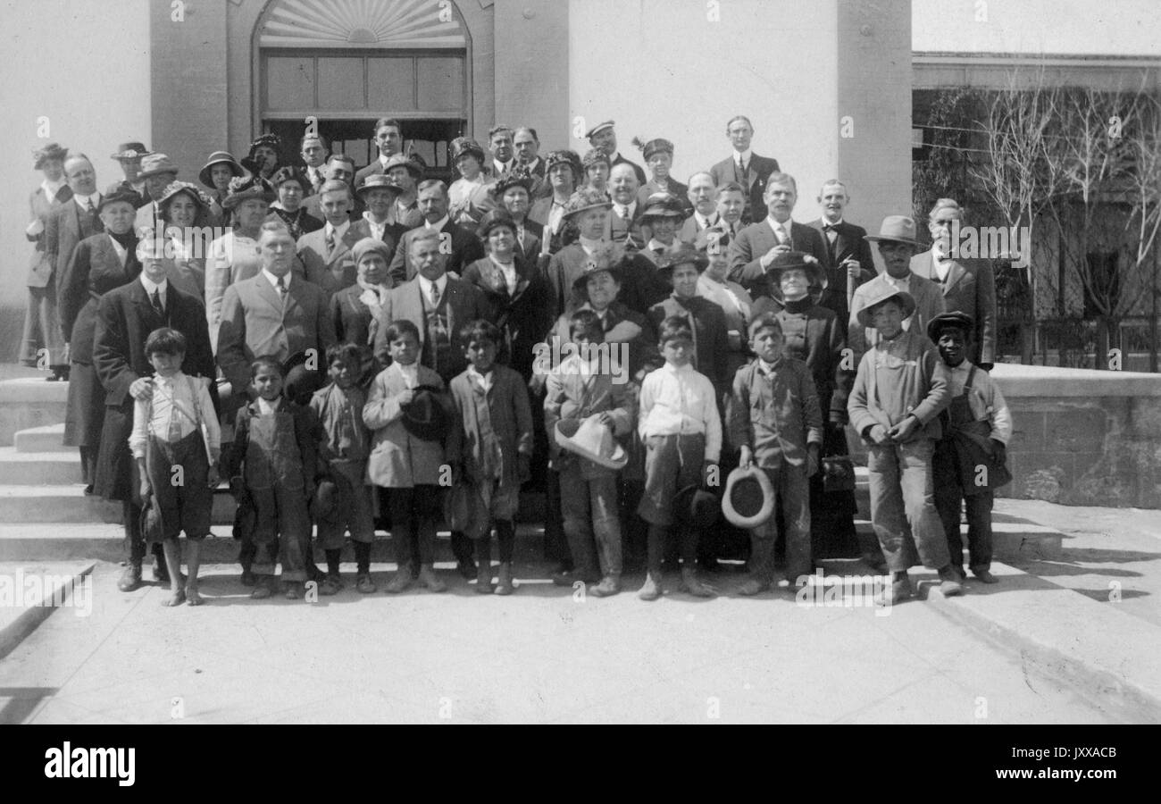 Photo de paysage pleine longueur d'adultes et d'enfants tous debout dans les rangs, certains Afro-américains, tous habillés officiellement, 1920. Banque D'Images