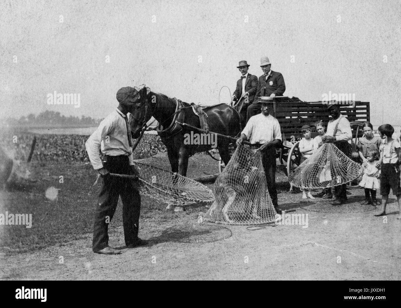 Trois chiens de traîneau américains, dont un contient un chien sauvage, et plusieurs jeunes enfants, se tiennent devant un wagon ouvert conduit par deux autres ouvriers et porté par un cheval, sur un sentier extérieur, 1912. Banque D'Images