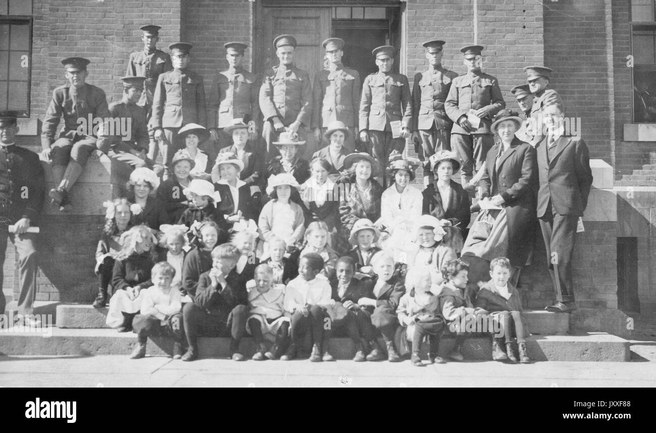 Soldats américains sont alignés en haut des marches de l'extérieur d'un bâtiment en face d'eux, assis sur les marches sont des mères et leurs enfants, 1920. Banque D'Images