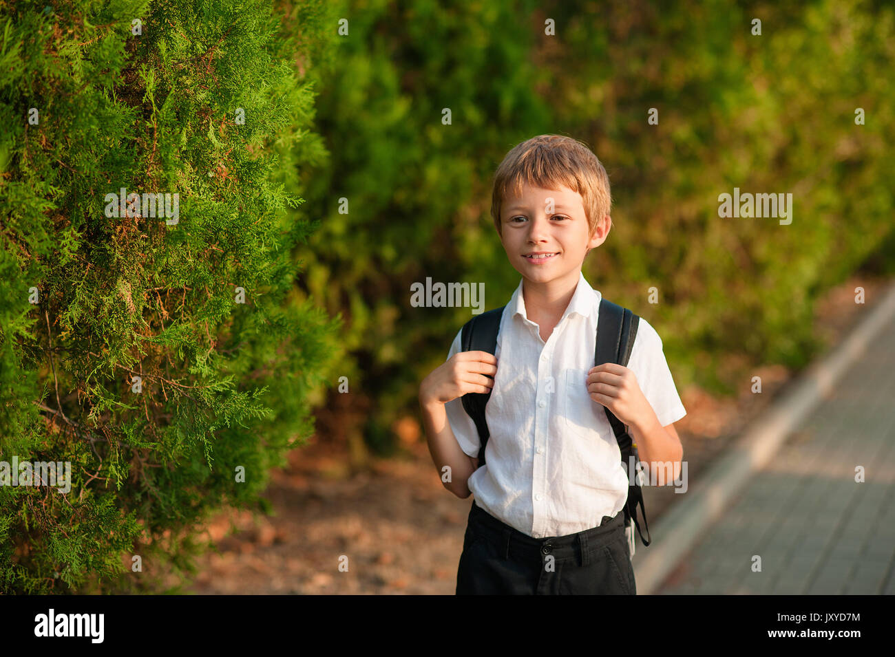 Écolier souriant avec sac d'école fonctionnant en journée ensoleillée. Garçon allant à la maison de l'école. Banque D'Images