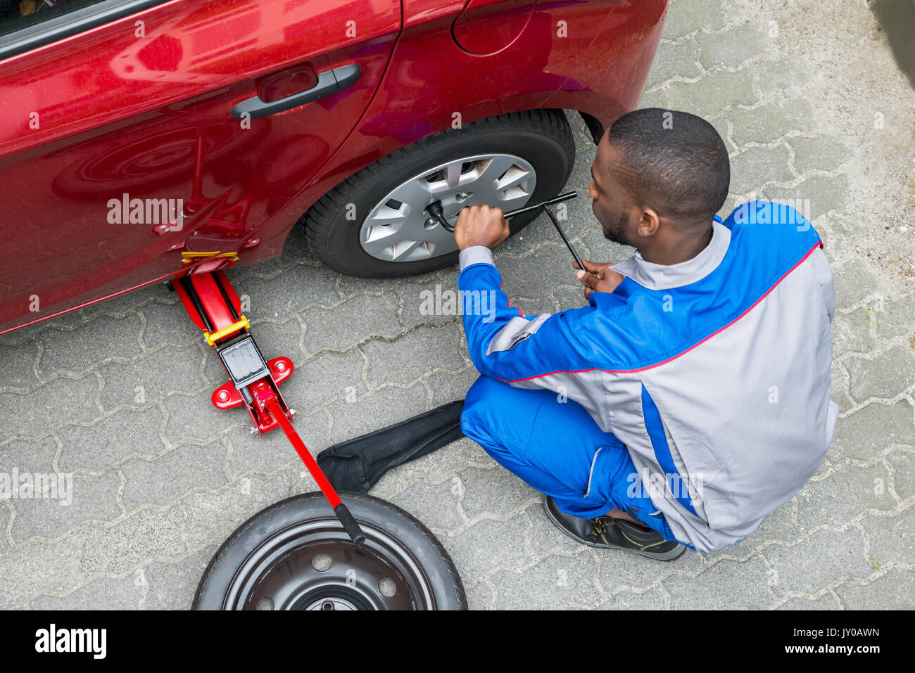 Jeune Mécanicien de l'Afrique de l'évolution de pneu d'une voiture avec une clé Banque D'Images