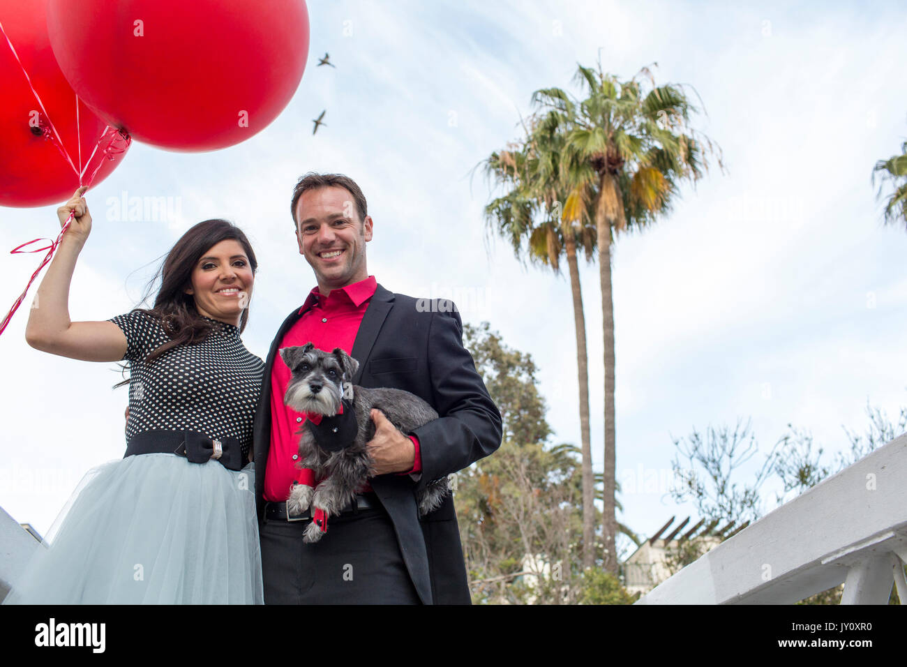Smiling couple holding dog et red balloons Banque D'Images
