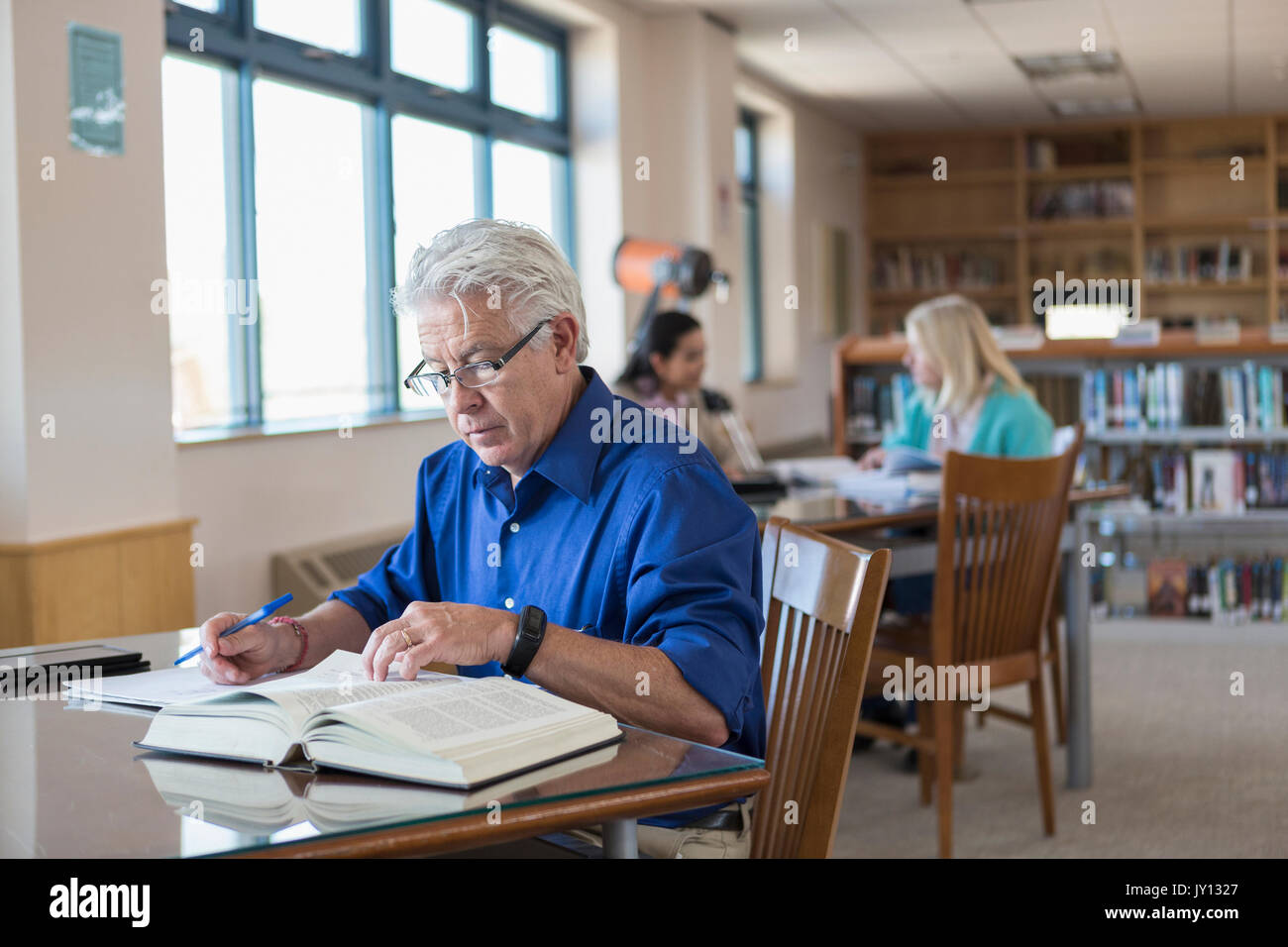 Older Man reading book in library et la rédaction de notes Banque D'Images