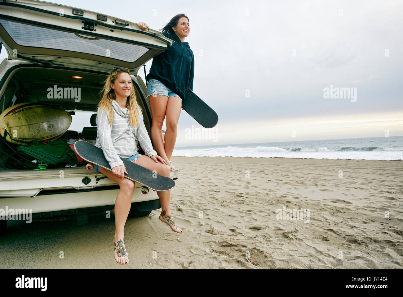 Les femmes de race blanche en voiture éclosent à beach holding skateboards Banque D'Images